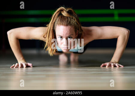 Sporty young woman doing push-ups in exercise room Stock Photo