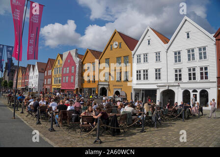 Tourists sit in the sun in outdoor bars and cafes in the old wharf and traditional wooden buildings in the Bryggen quarter of Bergen, UNESCO, Norway Stock Photo