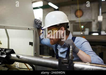 Serious manual worker in protective workwear and protective glasses working on lathe in the plant Stock Photo