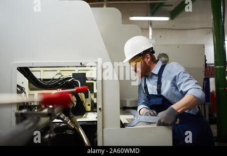 Serious technician in protective workwear and glasses repairing the machine with big wrench in the plant Stock Photo