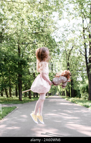 Cute little girl in a park jumping with her hobbyhorse Stock Photo