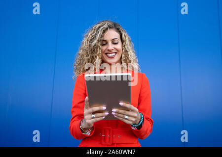 Portrait of young woman wearing red dress in front of blue background using digital tablet Stock Photo