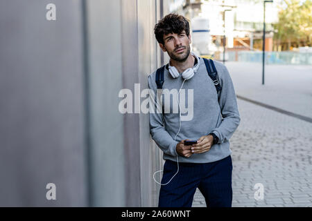Man holding cell phone leaning against a wall Stock Photo