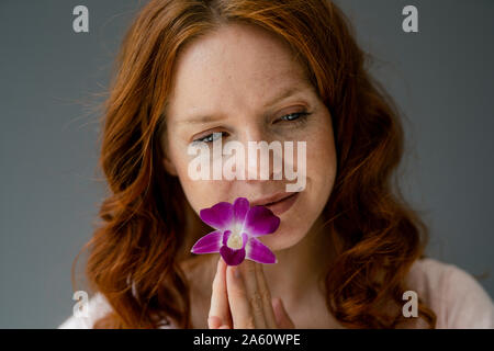 Portrait of redheaded woman with purple orchid blossom Stock Photo