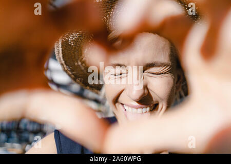 Woman with straw hat, looking into the sun, making heart shaped finger frame Stock Photo