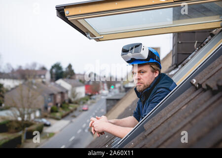 Architect with VR goggles on his safety helmet, looking out of rooflight Stock Photo