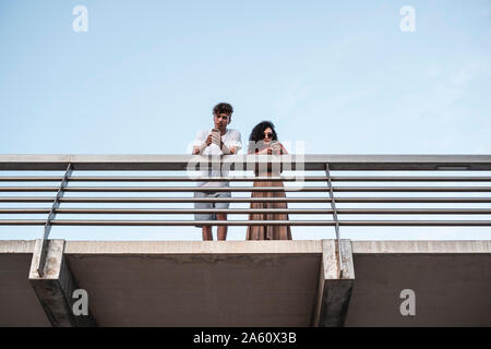 Young couple standing on bridge, using smartphones Stock Photo