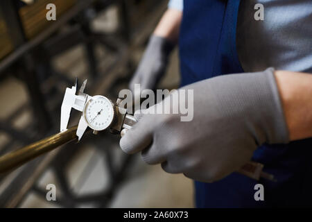 Close-up of worker in protective gloves holding iron pipe and measuring it with special instrument of measurement Stock Photo