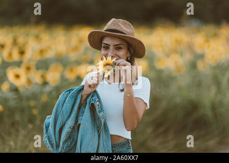 Portrait of young woman with blue denim jacket and hat in a field of sunflowers Stock Photo