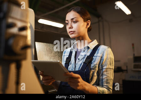 Female worker in overalls using digital tablet in her work and watching for the process while working in the plant Stock Photo