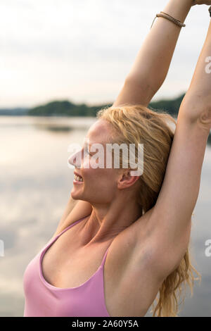 Happy young woman raising her arms at a lake Stock Photo
