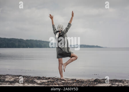 Senior woman looking at sea, standing on one leg, rear view Stock Photo