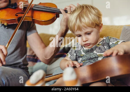 Portrait of toddler testing ukulele while his father playing violin Stock Photo