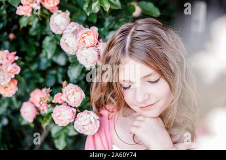 Portrait of girl with eyes closed beside pink rosebush Stock Photo
