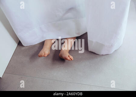 Legs and feet of little boy, hiding behind curtain Stock Photo