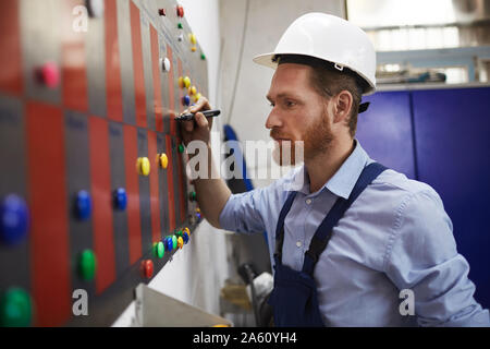 Foreman in work wear standing near the blackboard and making the timetable of his workers Stock Photo
