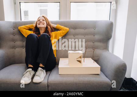 Happy woman sitting on couch next to architectural model Stock Photo