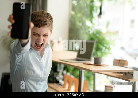 Portrait of screaming businesswoman holding cell phone in a cafe Stock Photo