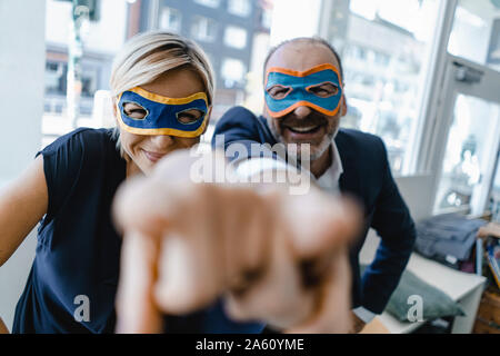 Businessman and woman, wearing super hero masks, pointing at camera Stock Photo