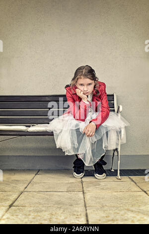 Portrait of unhappy girl wearing red leather jacket and tutu sitting on bench Stock Photo