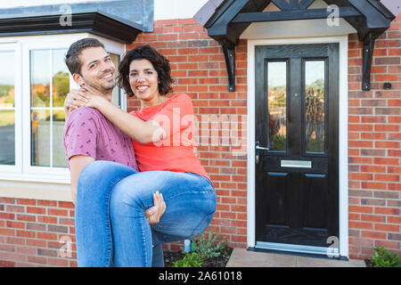 Happy man carrying woman in front of their new home Stock Photo
