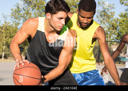 Young men playing basketball and dribbling ball on sports ground Stock Photo