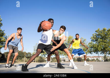 Young men playing basketball and dribbling ball on sports ground Stock Photo