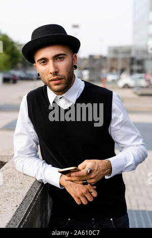 Porrtait of young man with cell phone dressed in black and white leaning on wall Stock Photo