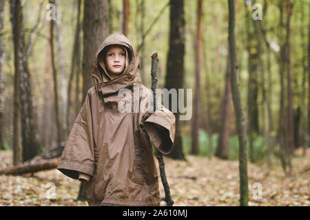 Portrait of boy wearing brown rain coat standing in autumnal forest Stock Photo