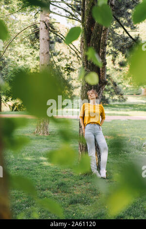 Young woman leaning against a tree in park Stock Photo