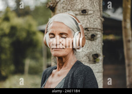 Senior woman relaxing in nature, listening music with headphones Stock Photo