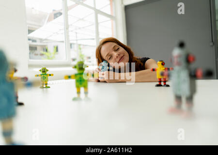 Portrait of redheaded businesswoman in a loft with miniature robots on desk Stock Photo