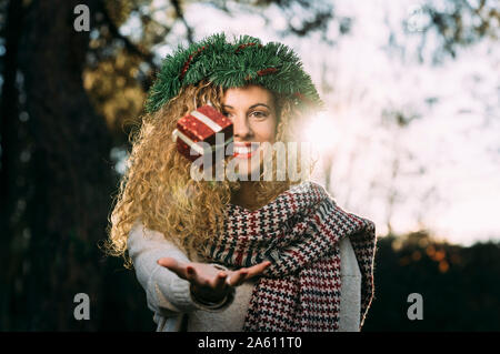 Portrait of smiling young woman with Christmas wreath on her head juggling with Christmas present Stock Photo