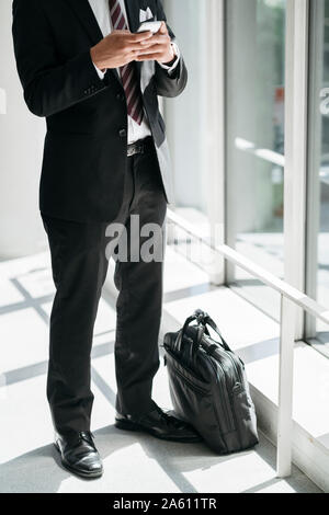 Low section of businessman using cell phone at the window Stock Photo