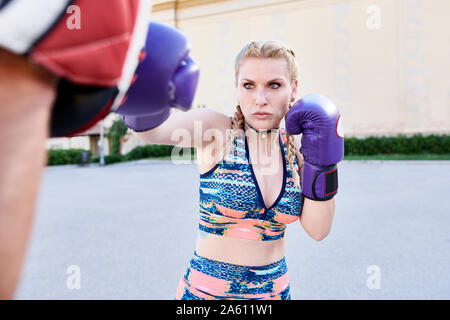 Focused young woman boxing with fitness coach outdoors in the city Stock Photo