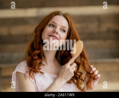 Portrait of smiling redheaded woman brushing her hair Stock Photo