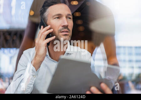 Portrait of businessman with tablet on the phone behind windowpane in a cafe Stock Photo