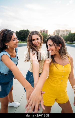 Three happy female friends stacking their hands Stock Photo