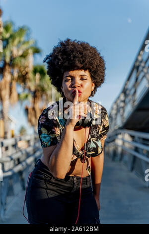 Female Afro-American with headphones, finger on lips Stock Photo