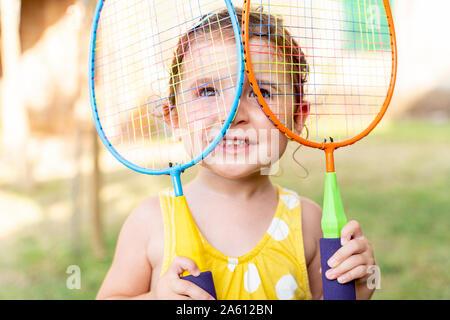 Little girl playing with colorful badminton rackets outdoors in summer