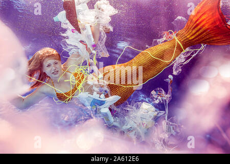 Teenage mermaid girl surrounded by plastic waste under water Stock Photo