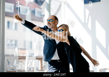 Businessman and woman wearing super hero masks, pretending to fly Stock Photo
