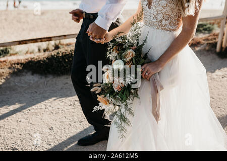 Close-up of bride and groom walking on path at the coast Stock Photo