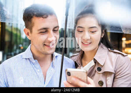 Happy couple with umbrella and celll phone in Ginza, Tokyo, Japan Stock Photo