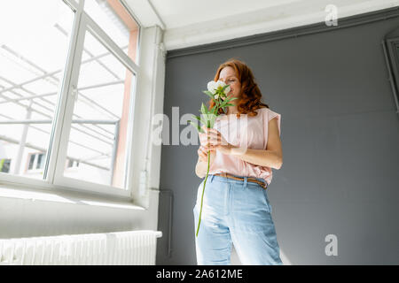 Redheaded woman smelling white peony