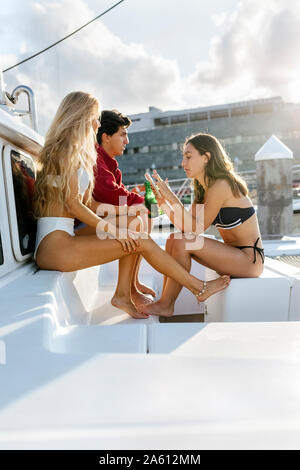 Three young friends enjoying a summer day on a sailboat, woman using smartphone Stock Photo