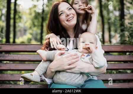 Smiling mother with her two kids eating cookies in the park Stock Photo