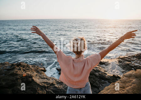 Rear view of young woman at the sea with raised arms, Sunset Cliffs, San Diego, California, USA