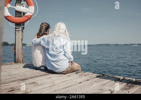 Mother and daughter looking at the sea, sitting on jetty, rear view Stock Photo