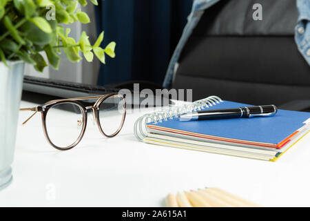 Home office desk and empty chair. Notebook, pen and glasses on desk. Working at home, freelance, successful business concept Stock Photo